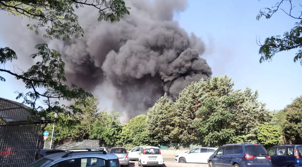 nor de fum negru care se ridică peste copaci și mașini, în Via dei Gordiani, Roma, Italia. în partea de jos a imaginii se poate evdea o stradă asfaltată plină cu mașini