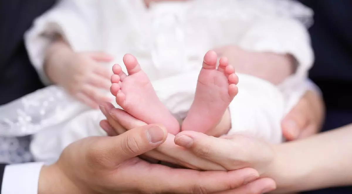 Un prim-plan arată picioarele mici ale unui bebeluș, ținute în mână de părinți
