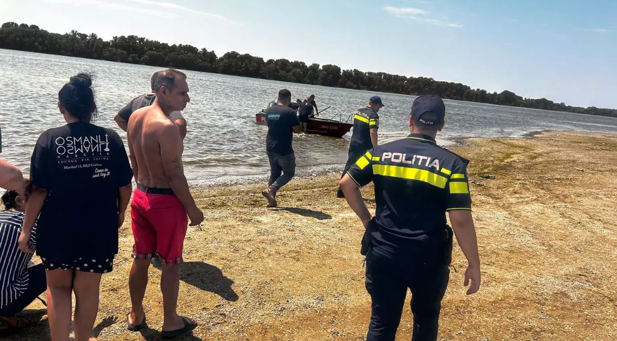 doi ofițeri de poliție, îmbrăcați în uniforme negre cu înscrisuri verzi fosforescent, alături de alți martori. stau în apropierea unei bărbați poziționate pe o plajă neamenajată din zona Gostinu, județul Giurgiu