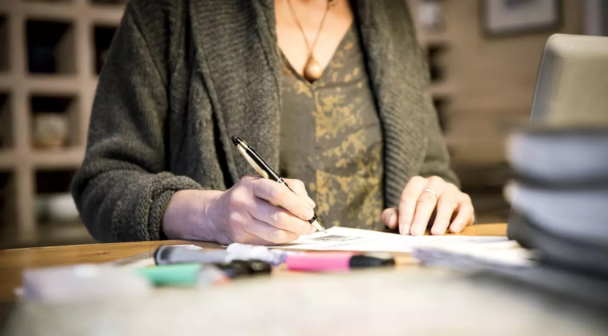 Imagine cu o femeie care ține un pix în mână și are în fața un document