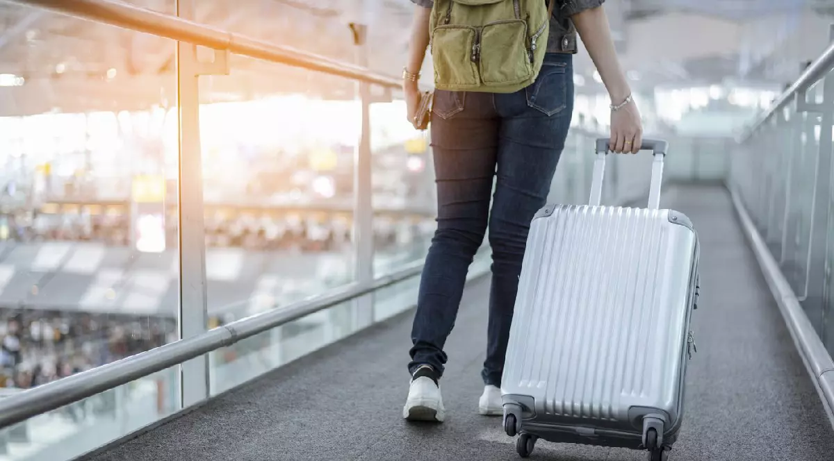 O femeie care călătorește cu valiza, urcând pe o scară rulantă într-un aeroport.