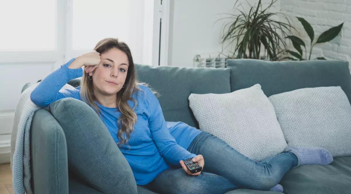 O femeie îmbrăcată în haine albastre care stă pe o canapea cu o telecomandă în mână