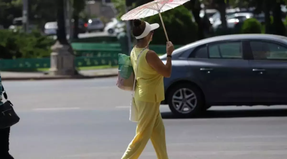 O femeie îmbrăcată în galben, care ține o umbrelă pe stradă
