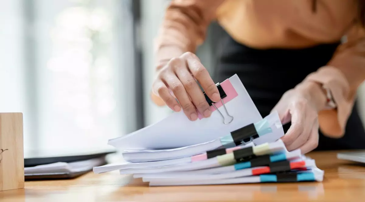 Persoana care numără un tens de dosare afalt pe birou