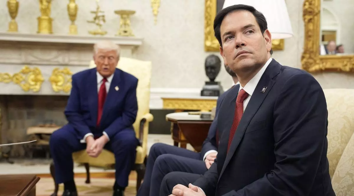 Marco Rubio întoarce capul și ascultă în timp ce stă pe o canapea, iar în fundal Donald Trump vorbește stând într-un fotoliu de la Casa Albă, aprilie 2025
