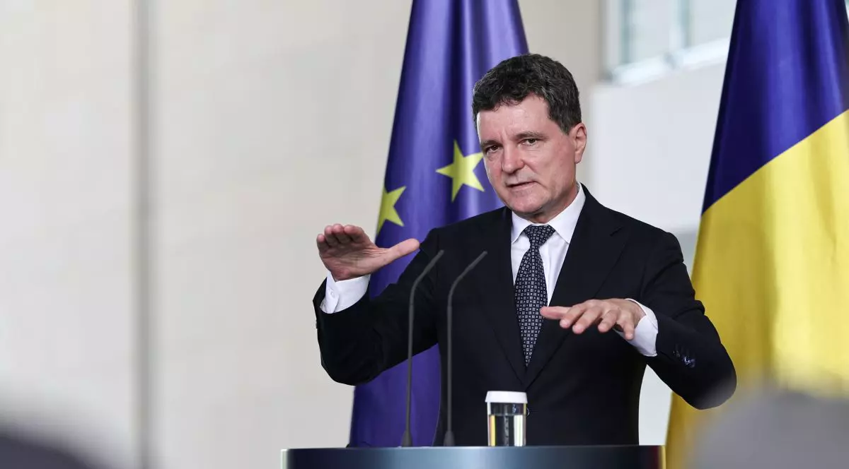 Nicușor Dan vorbește în timpul unei conferințe de presă stând la pupitru și folosind mâinile ca să explice, având pe fundal steagurile României și UE, iulie 2025