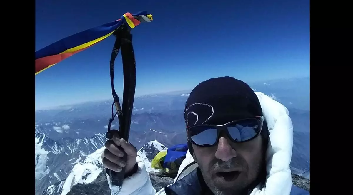 Horia Colibășanu, pe vârful Nanga Pabat din Pakistan, cu o căciulă neagră în cap și ochelari reflectorizanți de schi, îmbrăcat cu o geacă albă, ținând în mână un steag al României
