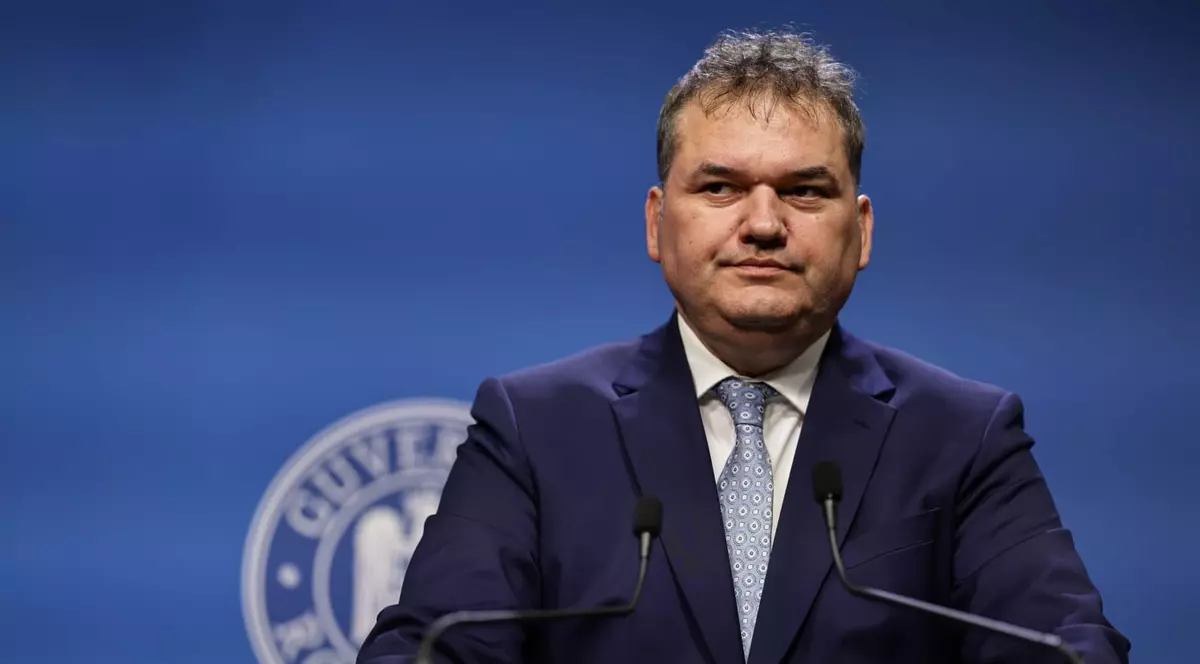 Cseke Attila, îmbrăcat într-un sacou bleumarin, o cămașă albă și o cravată gri, stând în fața unui pupitru cu două microfoane, cu emblema guvernului româniei în spate