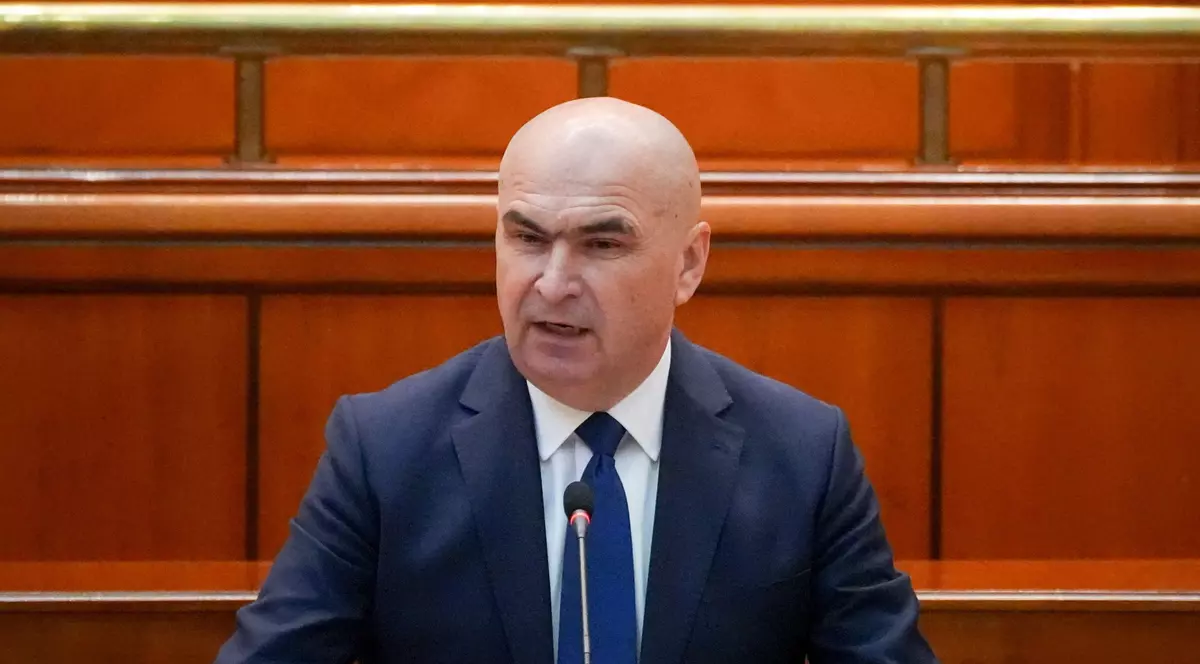 Ilie Bolojan surprins în timp ce vorbește la microfon la Palatul Parlamentului, în iunie 2025. Poartă un sacou albastru închis, o cravată de aceeași culoare și o cămașă albă