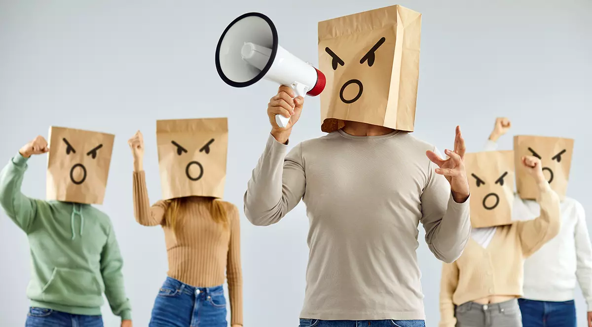 Bărbat cu emoticon furios pe cap strigă tare în difuzor alături de un grup de sprijin. Un grup de oameni cu pungi de hârtie cu emoticoane desenate pe ele scandează și cer acțiuni decisive