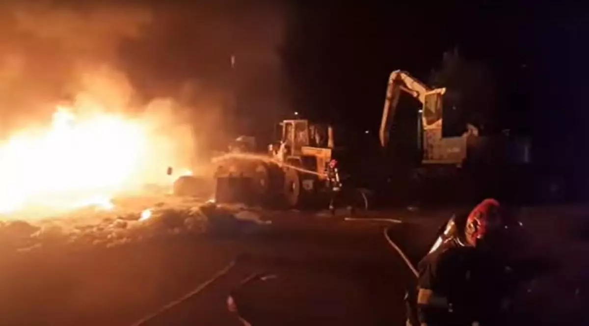 Pompierii cu furtunul de apă în timp ce încearcă să stingă flăcările care au cuprins o hală cu fier vechi și utilajele învechite.