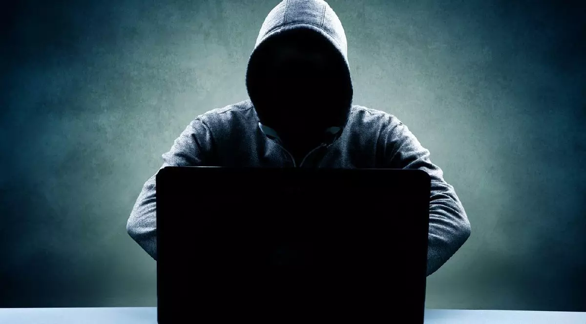 Bărbat în hanorac, cu fața ascunsă, stând în fața unui laptop