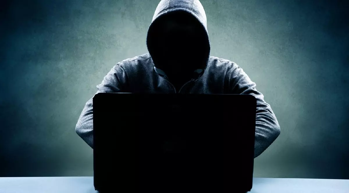 Bărbat în hanorac, cu fața ascunsă, stând în fața unui laptop