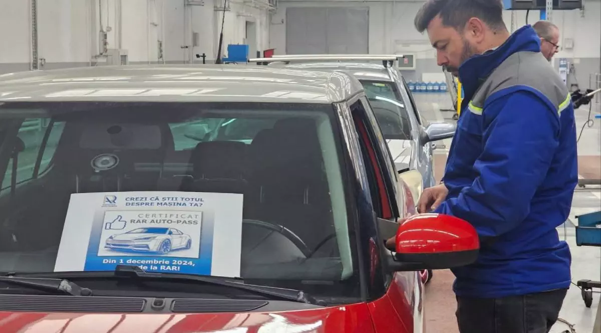 Inginer de la Registrul Auto Român (RAR), îmbrăcat în uniformă de culoare albastră, cu mânecă lungă, lângă o mașină roșie, care are un afiș în parbriz pe care sunt oferite informații despre certificatul RAR Auto-Pass