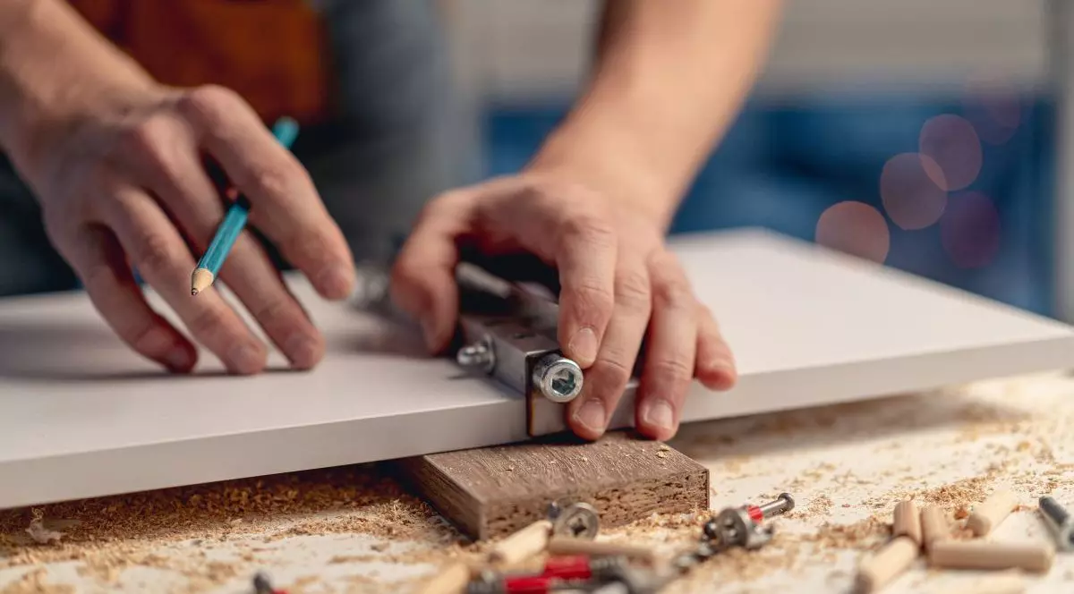 Un bărbat care lucrează cu creionul marcând găuri în timpul procesului de fabricare a mobilei din lemn în atelier