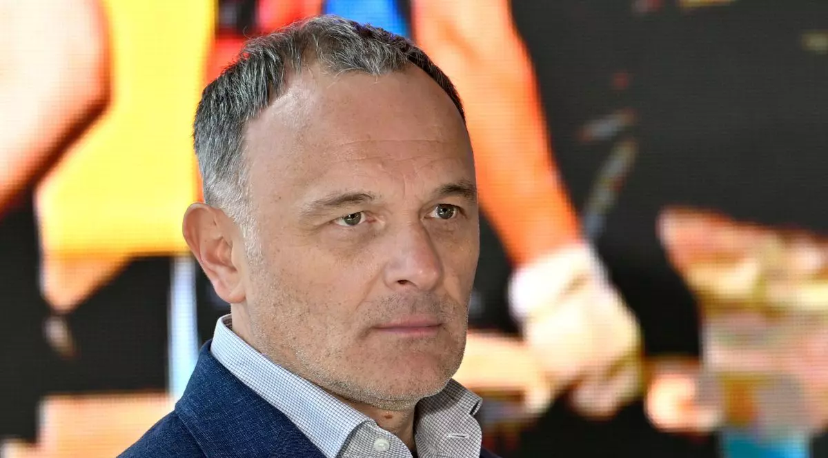 Karoly Borbely, șeful Hidroelectrica, îmbrăcat cu un sacou, o cămașă deschisă la primul nasture de sus, iar pe fundal blurat mai multe persoane
