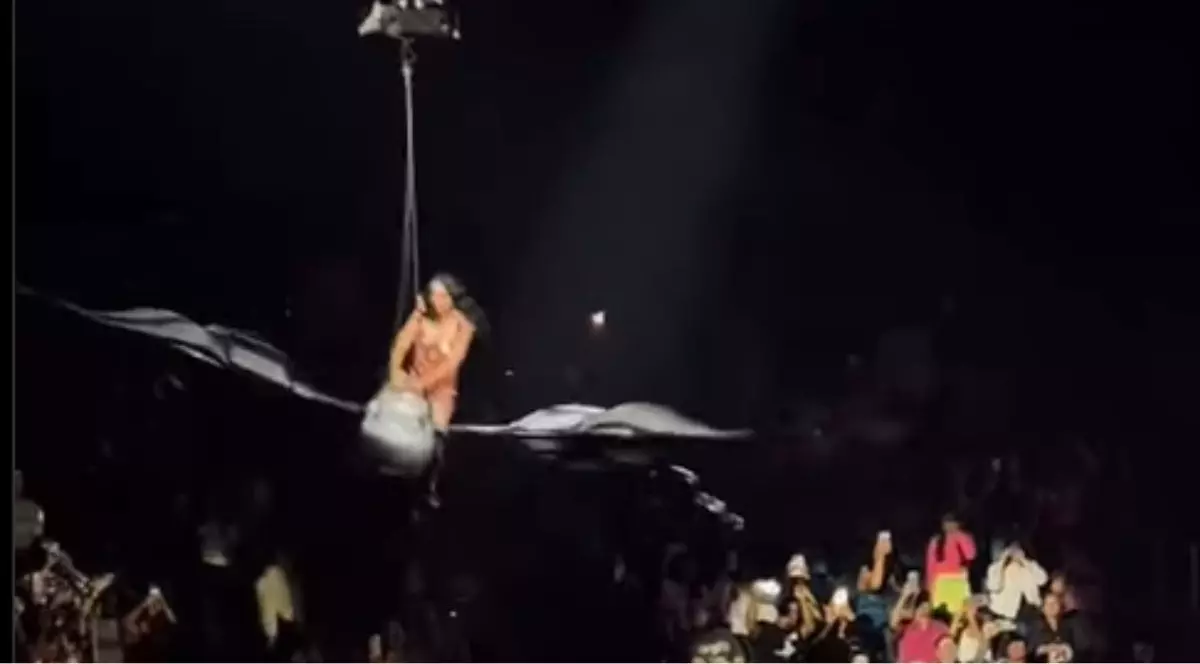 Katy Perry, îmbrăcată într-un body roșu cu pietre aplicate pe bust, stând în șezut pe un aparat zburător în formă de fluture în timpul unui concert în San Francisco, iulie 2025