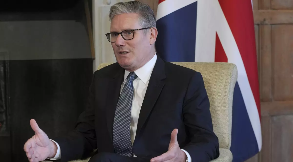 Imagine cu premierul Keir Starmer stând pe scaun. Poartă un costum negru, o cămașă albă și o cravată închisă la culoare cu buline albe