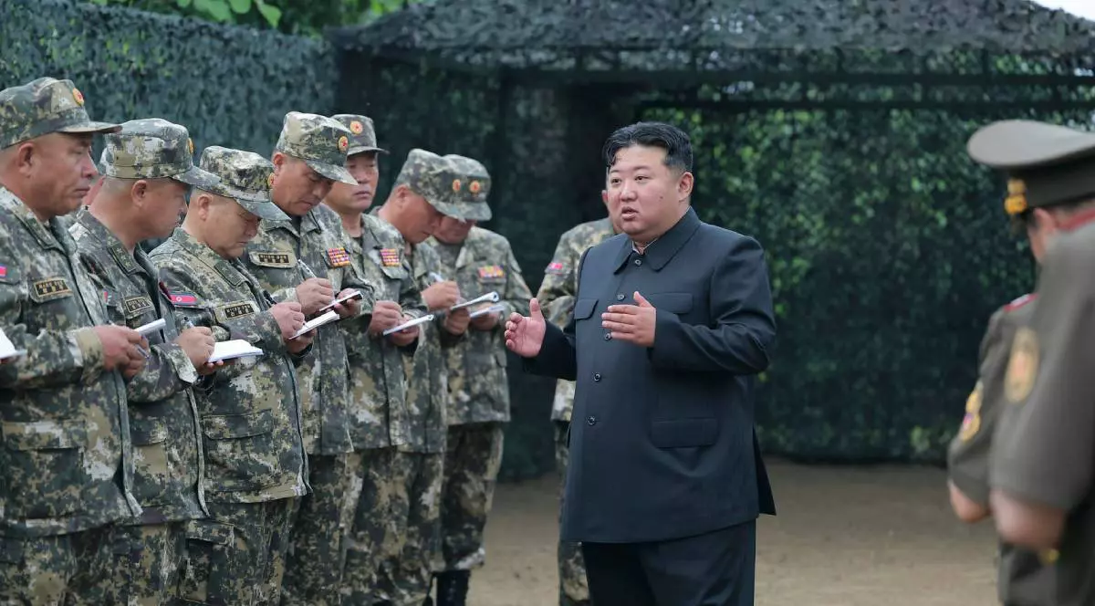 Kim Jong Un alături de soldații săi, în timp ce le vorbește. Poartă un costum negru iar militarii au uniforme