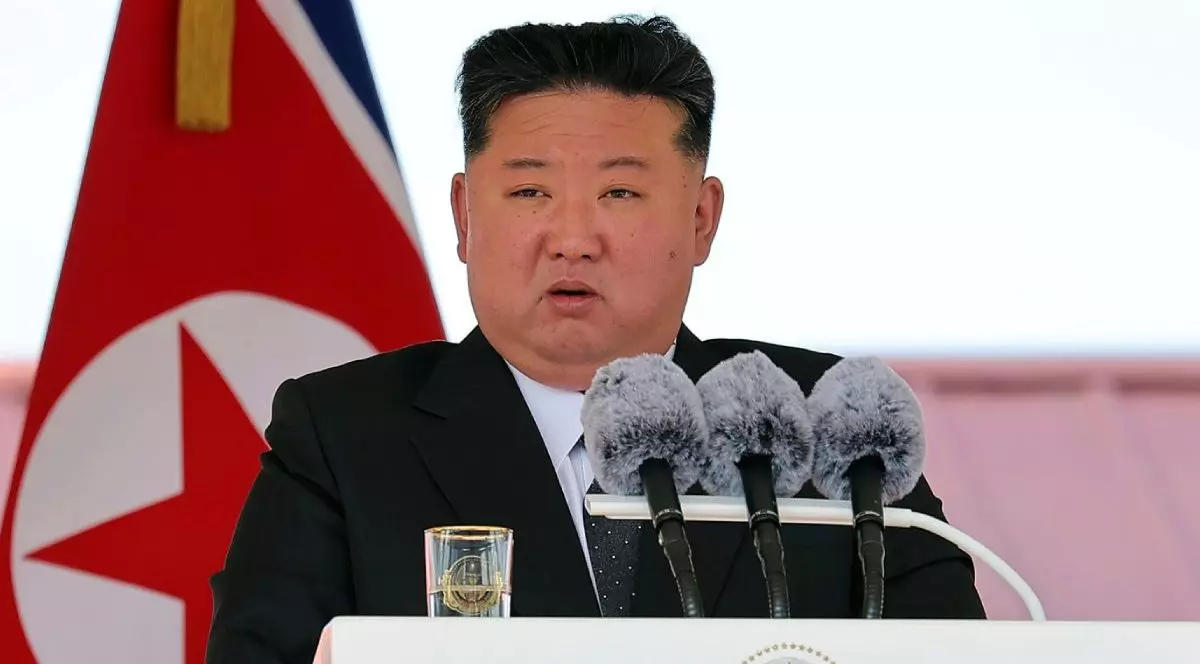 Liderul Nord Coreean Kim Jong Un, in sacou negru si camasa albă, in timp ce vorbește la un pupitru alb, cu trei microfoane pe el si un pahar alături, in cadrul unei conferinte, 12 iunie 2025, șantierul naval Rajin din Rason, Coreea de Nord