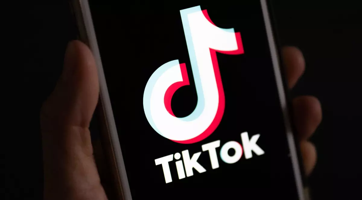 Imagine cu o mână în care se află un telefon mobil pe ecranul căruia este afișat logo-ul TikTok
