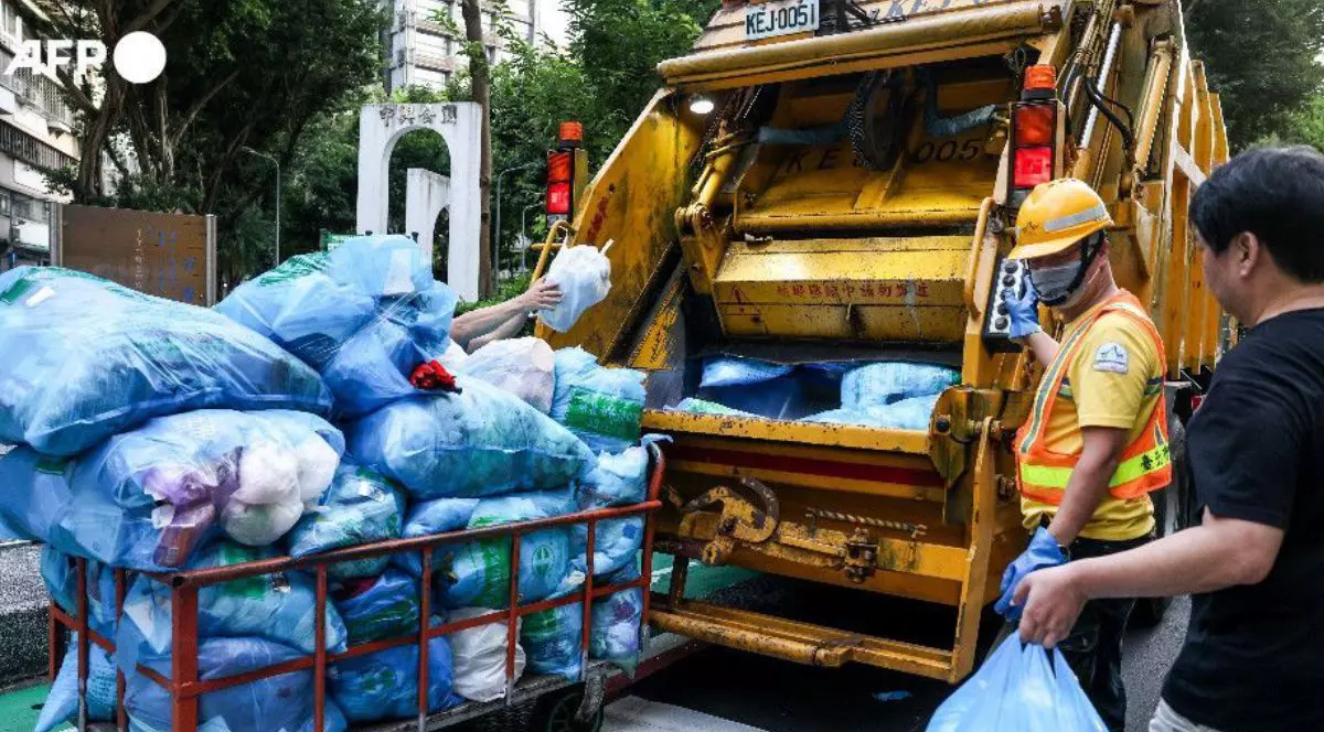 O masina de gunoi galbenă in Taipei, in timp ce ridică mai multi saci de gunoi albastri, langa masina un lucrător cu vesta și cascheta, langa el un bărbat cu un sac de gunoi in mana