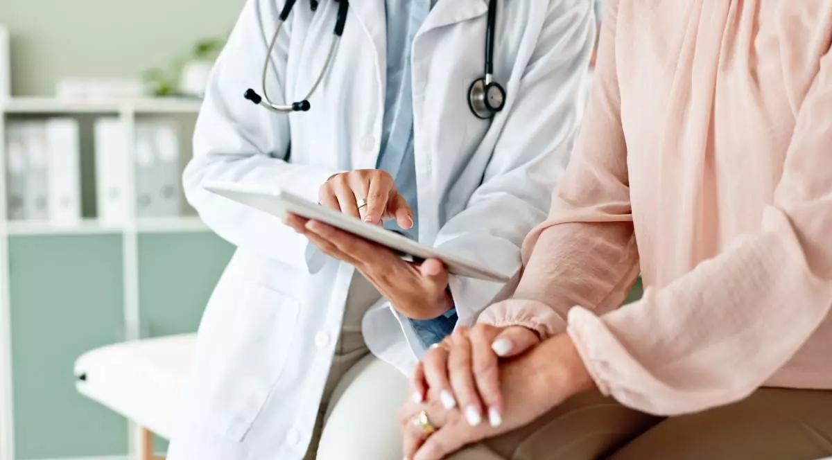 Un medic și o pacientă în timpul consolației, datele sunt digitalizate și pot fi verificate pe o tabletă pe care medicul îi arată ceva femeii.