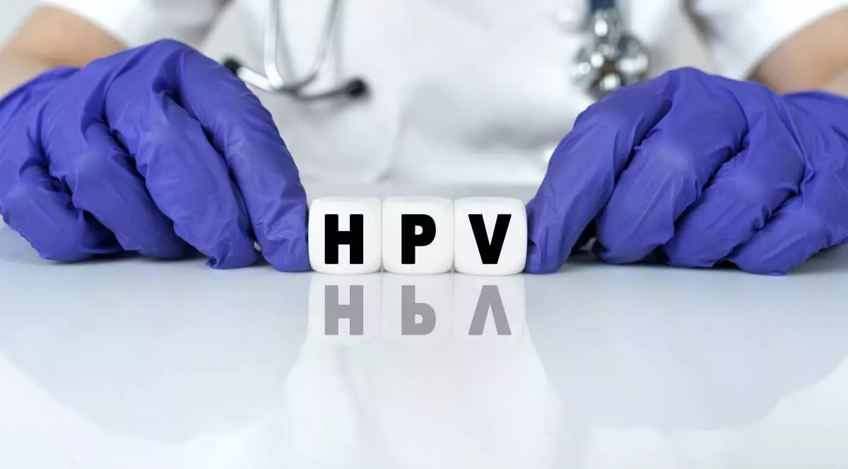 Vaccinarea anti-HPV prezentată de un medic în caginetul medical, doctorul poartă mânuși albastre și ține literele H,P și V pe masă
