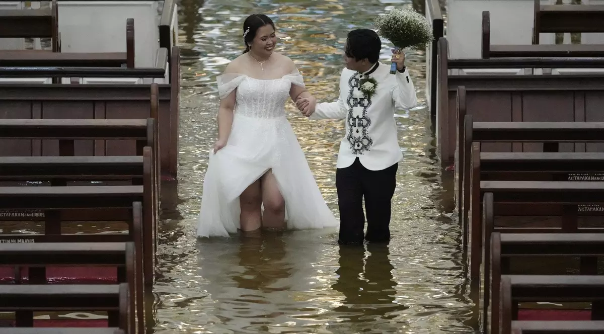 Jade Rick Verdillo (dreapta) și Jamaica Aguilar (stânga) surprinși în timp ce merg spre altar în biserica inundată, 22 iulie 2025. Mirele își ține mireasa de mână, iar în cealaltă are buchetul de flori