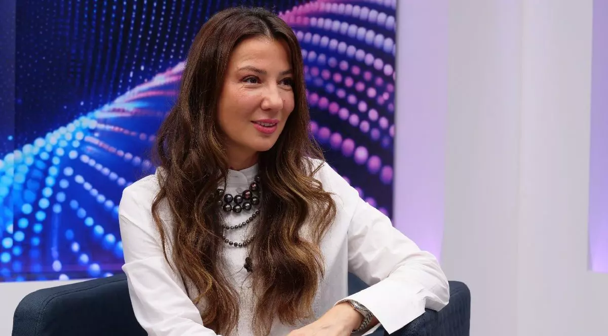Mirela Bucovicean, intr-o bluza alba, pe un fotoliu in studioul Libertatea. poarta un sirag de margele la gat sia re parul lung