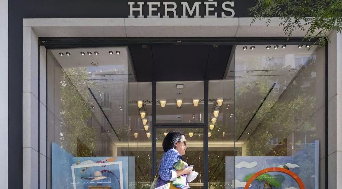 O femeie brunetă, cu cămașă albastră și ochelari de soare, trece pe lângă magazinul producătorului francez de haine de lux Hermes din Madrid, Spania, 10 iunie 2022