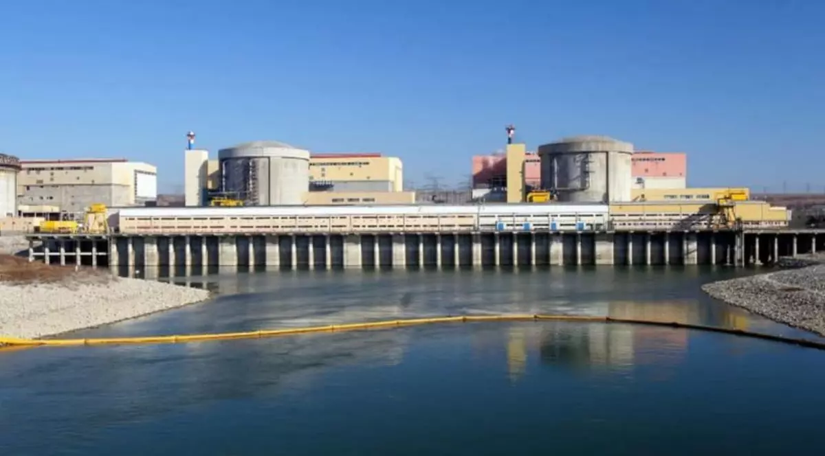 Imagine cu Nuclearelectrica, se vad mai multe cladiri in spate, cu un baraj construit in față și apă, apa este traversată de un furtun