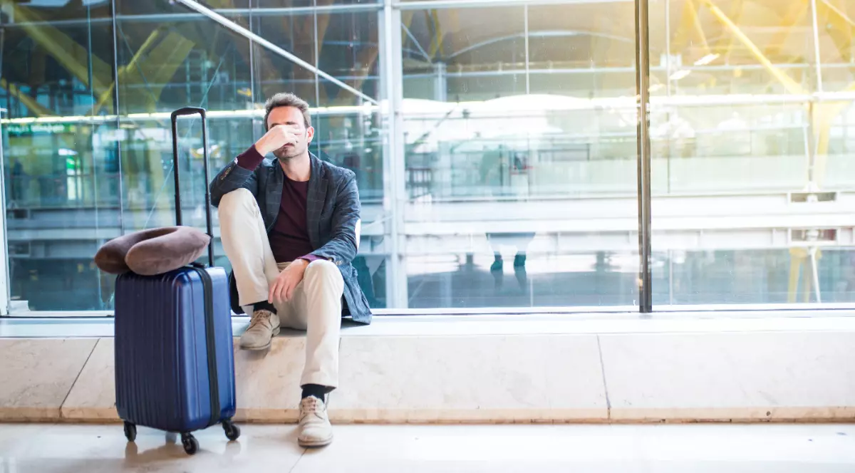 Un om care stă jos în aeroport, lângă un troller