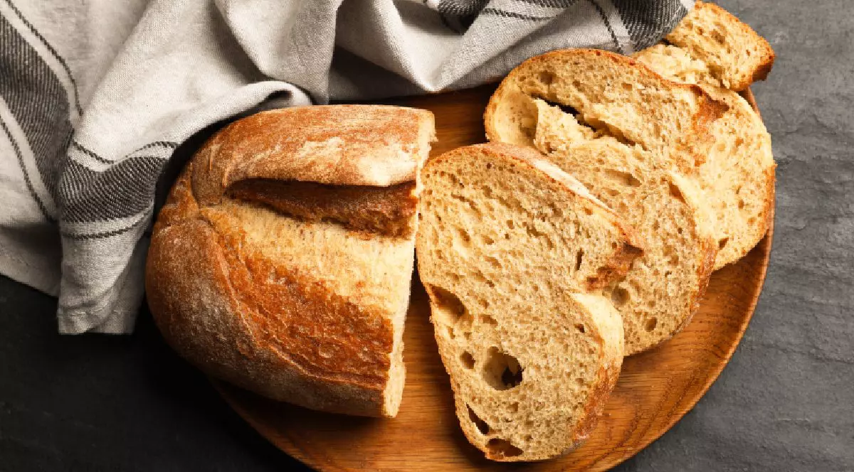 Bucăți de pâine proaspătă pe o masă neagră. Lângă, un prosop alb.