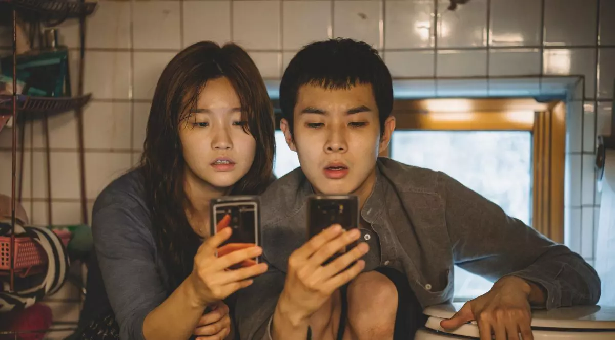 Imagine din filmul Parasite, regizat de Bong-Joon Ho, ]n care doi tineri stau pe telefoane.