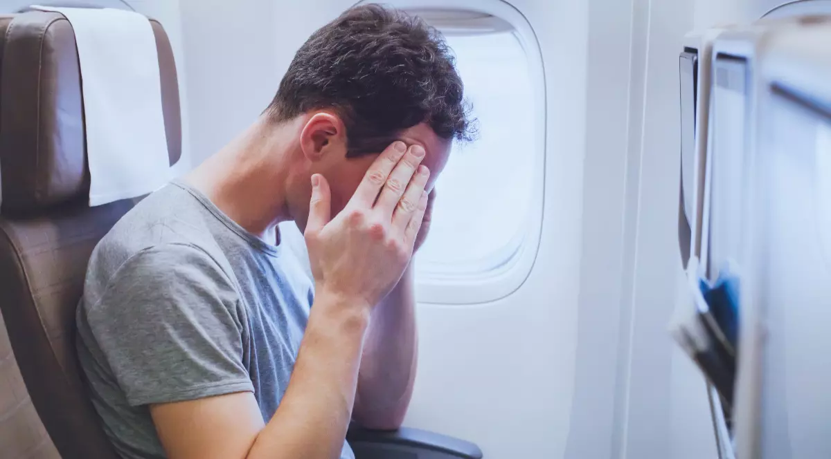 Un pasager aflat pe scaunul unui avion, cu mâinile pe tâmple, în semn de teamă de zbor