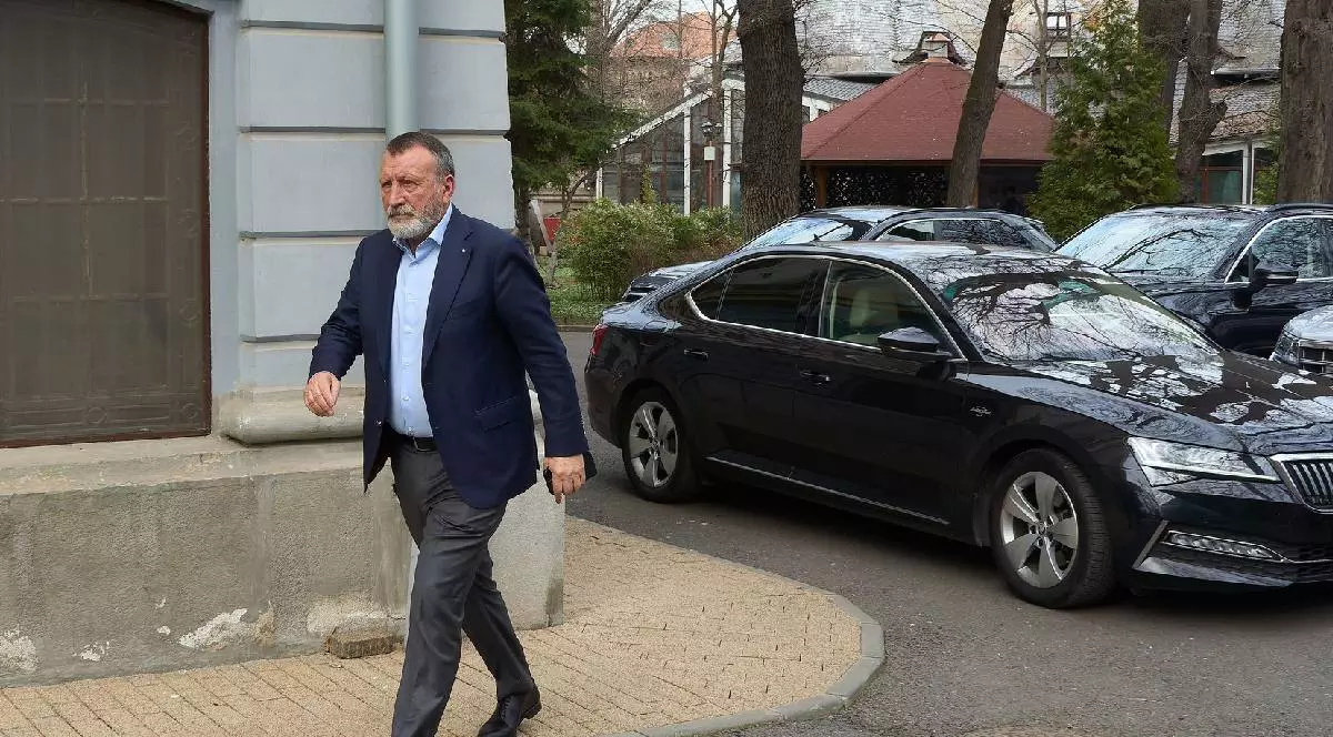 În imagine, Paul Stănescu se grăbește spre o ședință PSD, în spatele lui sunt parcate mai multe mașini de lux