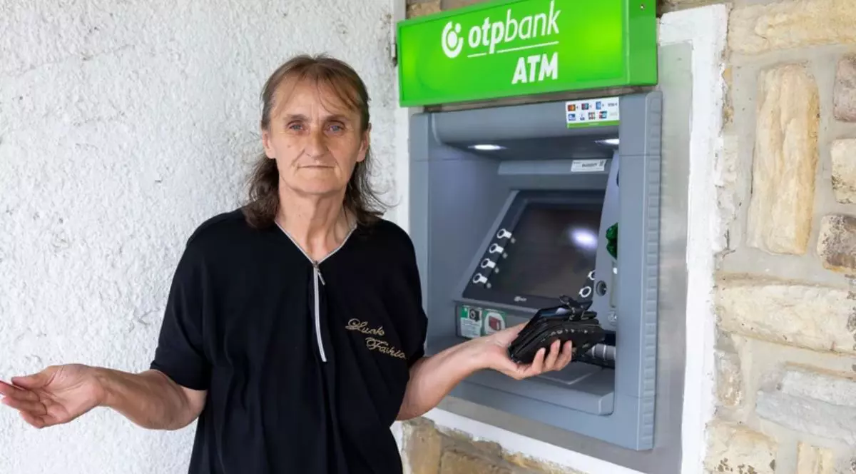 O femeie îmbrăcată în negru, cu un portofel negru în mână, lângă un bancomat al OTP Bank, cu logo-ul de culoare verde