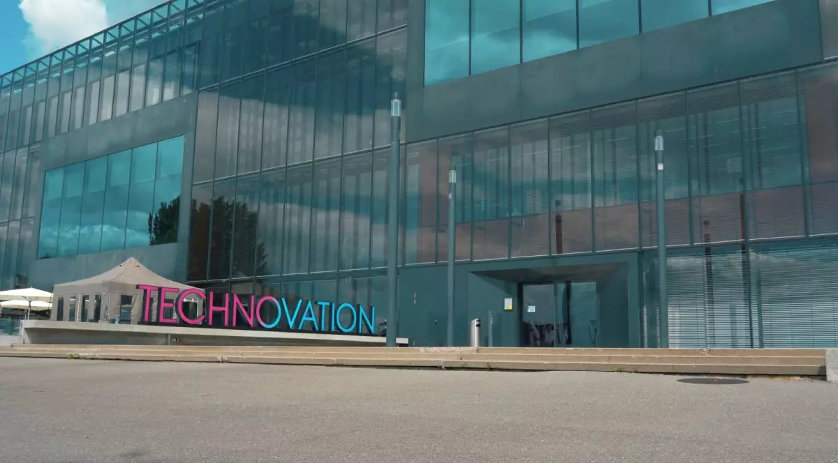 O clădire de sticlă din Neuchatel, Elvetia, în fața căreia e amplasat logo-ul conferinței Technovation, albatsru cu magenta, care aparține de Philip Morris International.