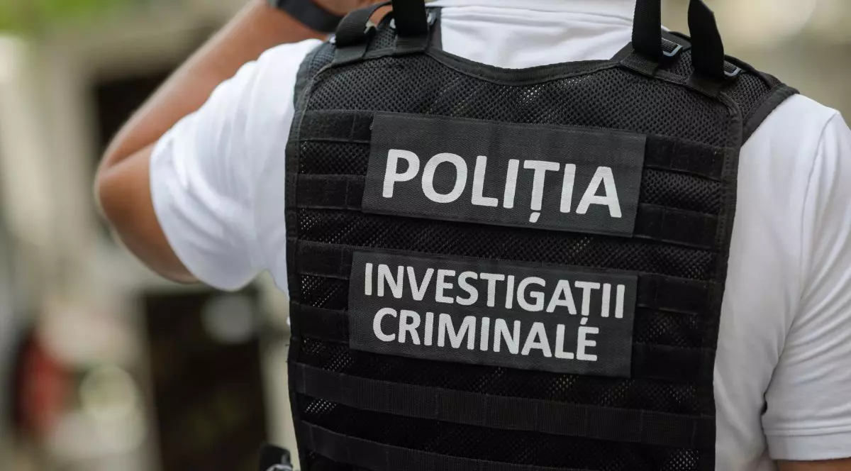 bărbat îmbrăcat într-o cămașă albă și o vestă neagră de poliție, cu textul „POLIȚIA INVESTIGAȚII CRIMINALE”, văzut de la spate