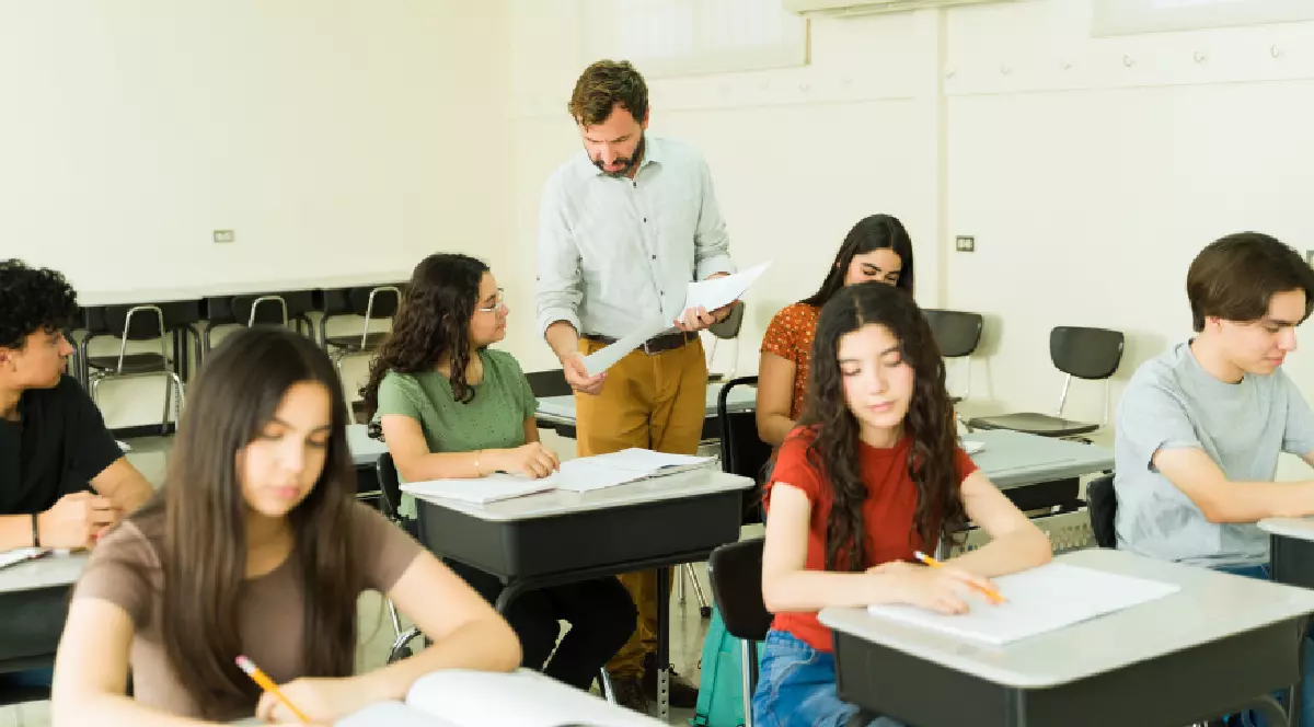 Profesor care supraveghează elevii de liceu în timp ce se concentrează pe examenele lor într-o clasă plină cu birouri și scaune