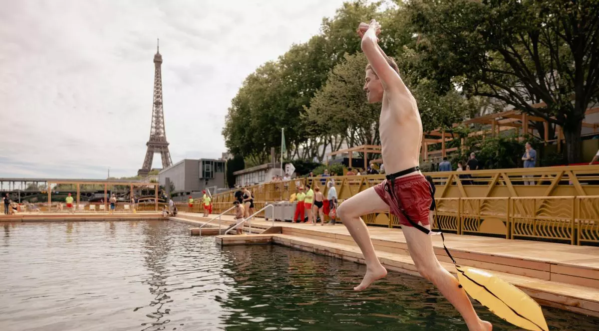 Un tânăr în slip și cu un flotor galben legat de talie sare în fluviul Sena, în timp ce pe fundal se distinge Turnul Eiffel din Paris, 5 iulie 2025
