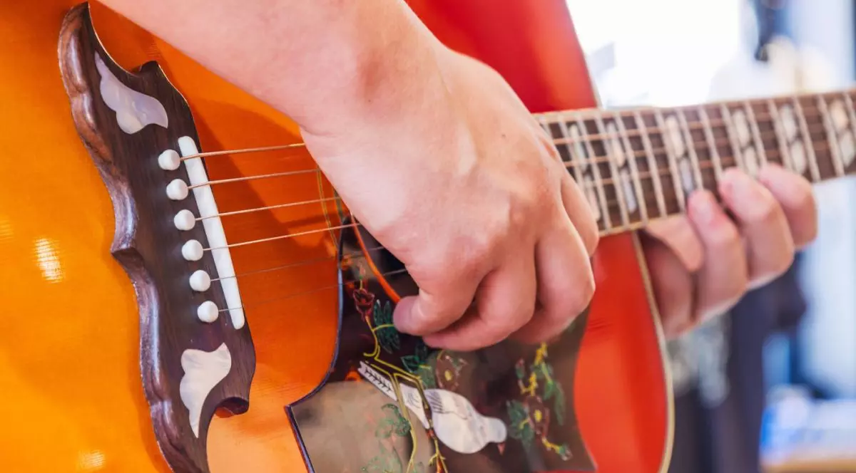 Mâna unui bărbat care folosește o chitară acustică