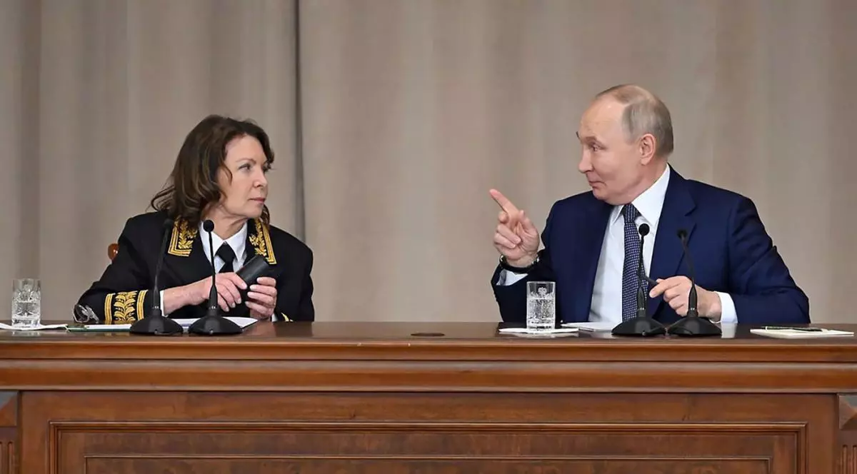 Vladimir Putin la costum și cu degetul arătător ridicat discută de la un pupitru cu Judecătoarea Irina Podnosova, mai 2025