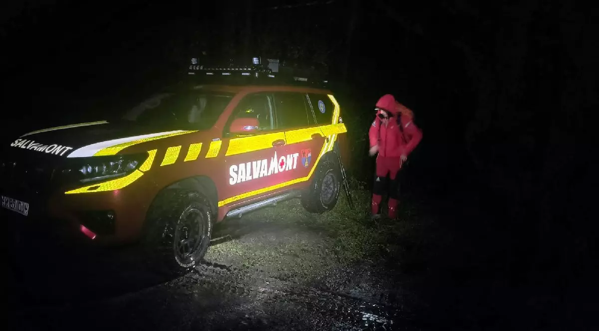 O mașină roșie, pe care scrie salvamont, lângă care este un salvamontist, fotografiată noaptea