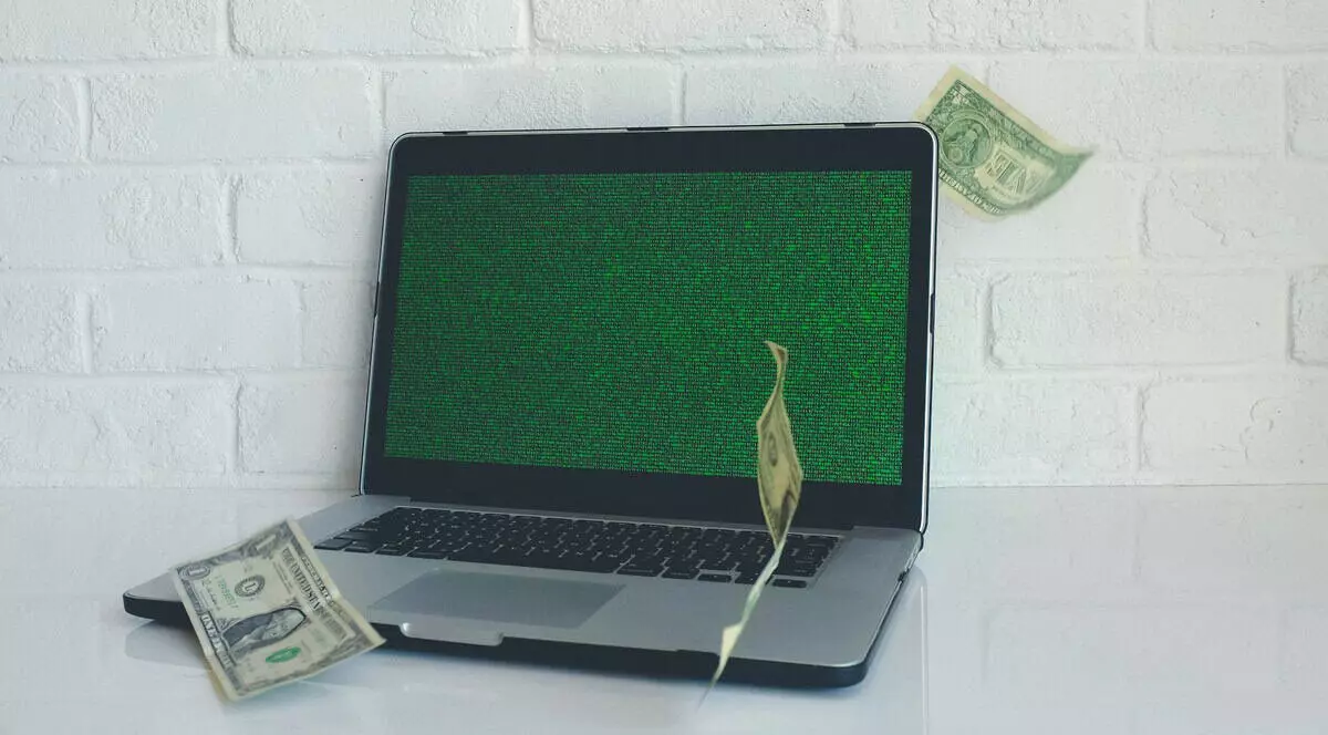 Credit online - poza cu un laptop asezat pe o masa alba, avand ecranul verde si cateva bacnote zburand pe langa el