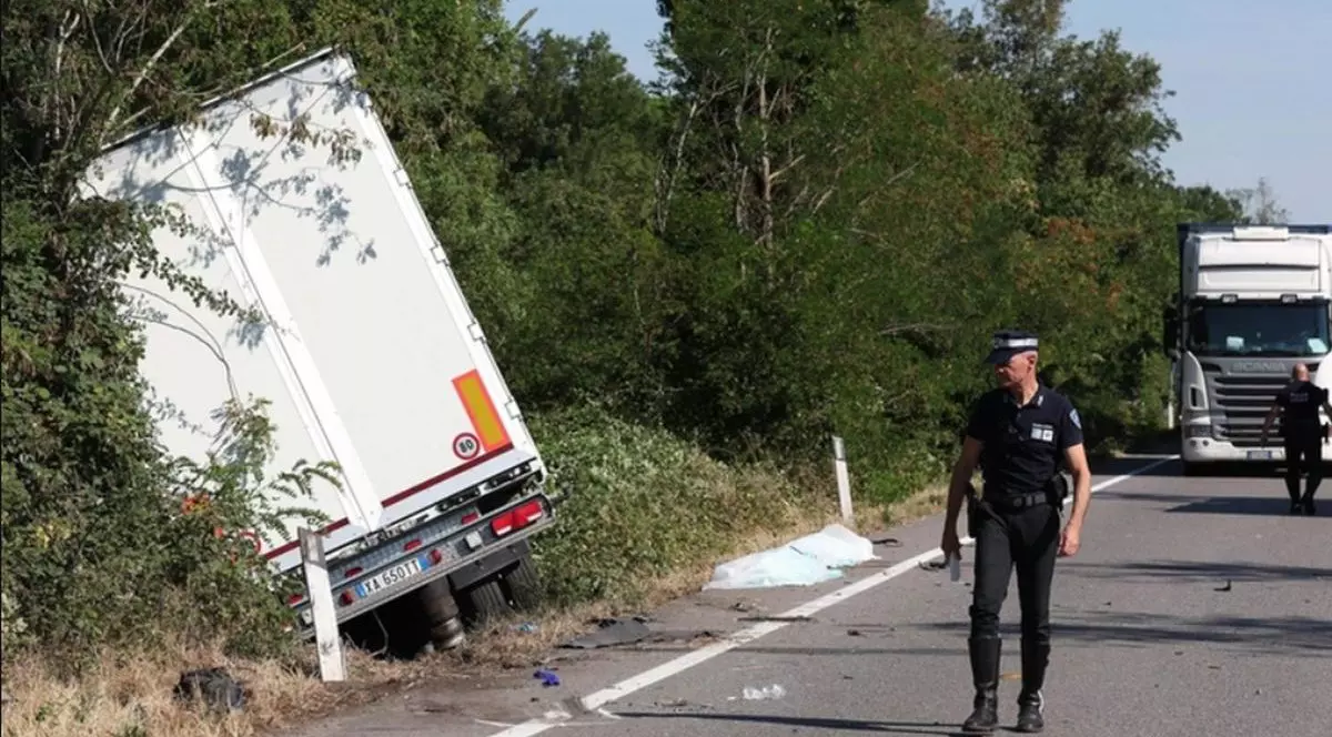 TIR-ul condus de un șofer român a ajuns într-un șanț, pe partea stângă, unde este și o zonă cu pomi, în față se vede un polițist, iar în spate pe șosea este un camion alb staționat și un bărbat