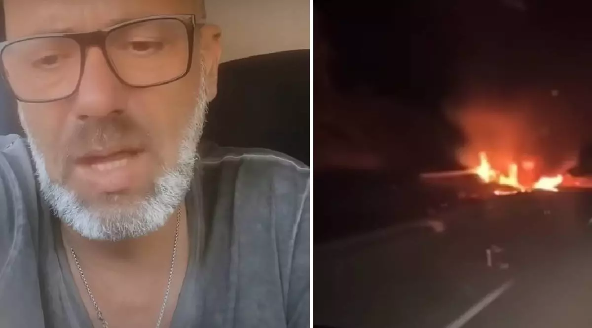 Un bărbat cu ochelari vorbește în fața camerei de luat vederi, în dreapta lui o mașină arde în noapte