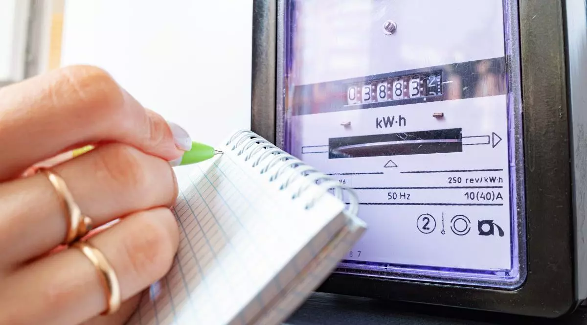 O femeie scrie cu un pic verde pe un carnețel indexul curentului electric, după ce a citit contorului de electricitate