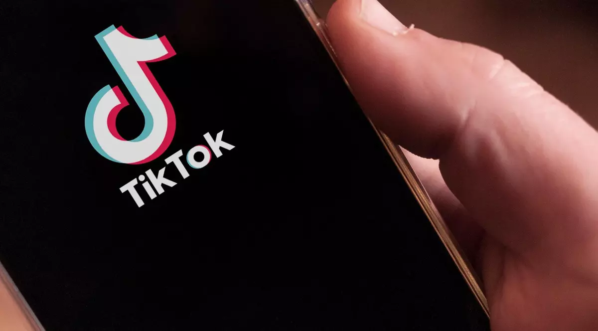 Imagine cu mâna unui bărbat în care se află un telefon. Pe ecran este afișat logo-ul TikTok